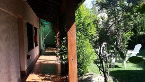 Zona exterior coberta amb paviment de rajoles, columnes de fusta i un petit jardí amb un arbre i una planta en test.