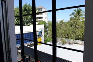 A view through a window with metal bars, featuring a building with a blue and white facade, a balcony, and a rooftop with a metal roof. - 7days Hotel Patan (Chiang Mai)