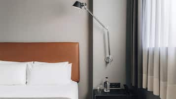 A hotel room with a bed, a nightstand, a lamp, a bottle, and a phone.