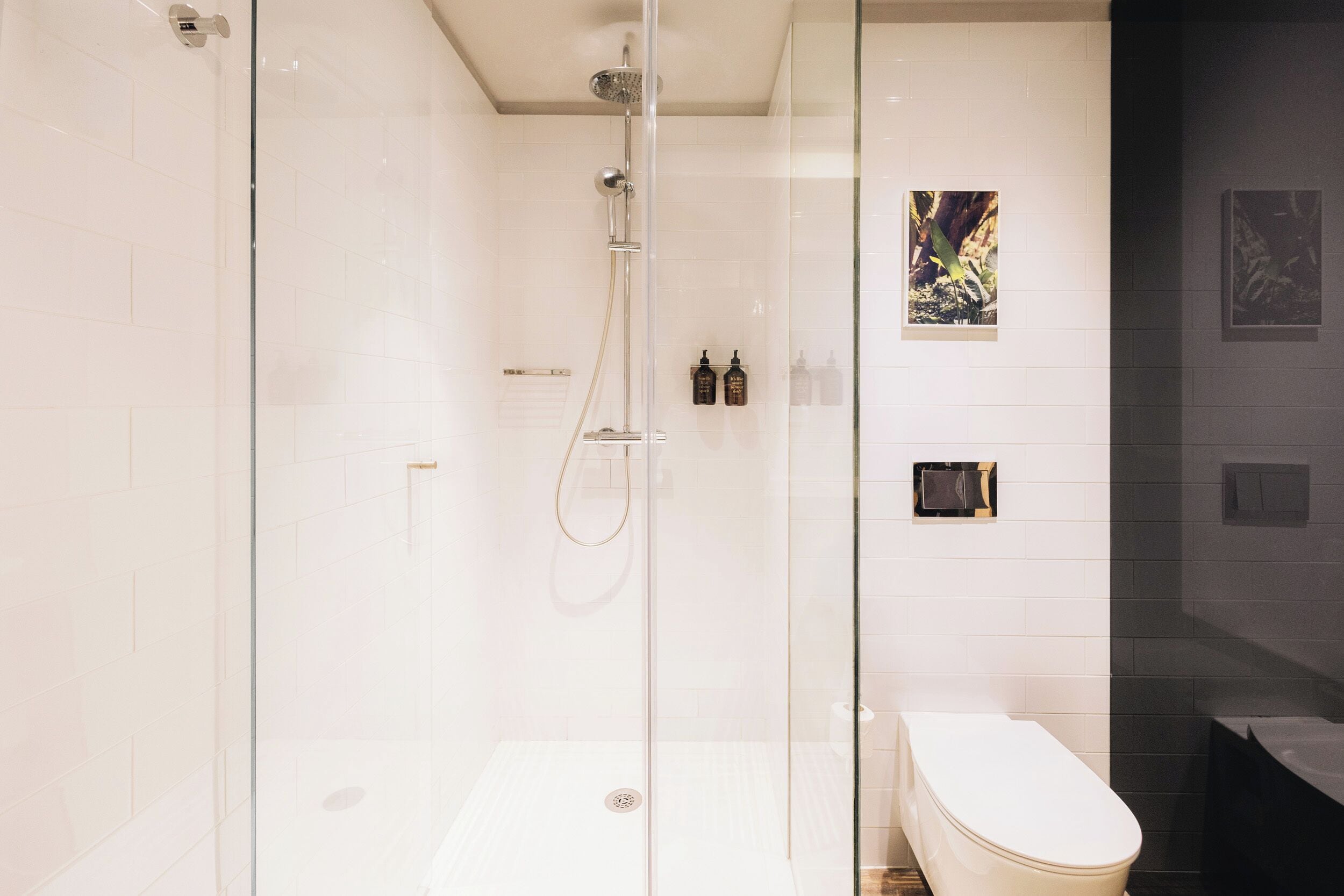 Un baño moderno con ducha acristalada, inodoro blanco y bañera oscura.