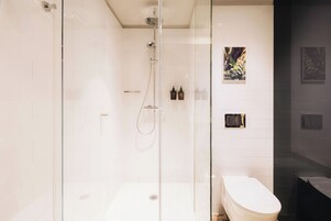 A modern bathroom with a glass-enclosed shower, a white toilet, and a dark bathtub.