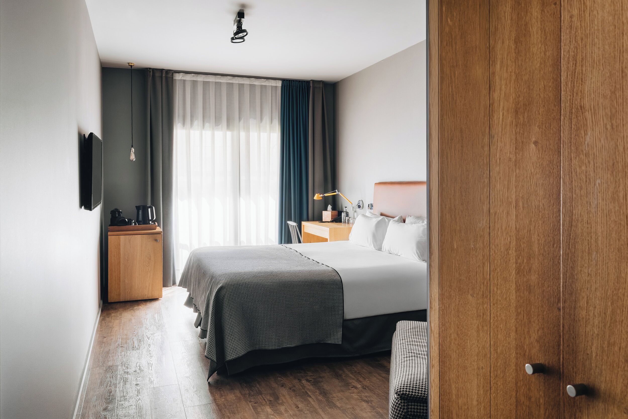 Una habitación de hotel moderna con una cama grande, mesita de noche, lámpara y un armario.