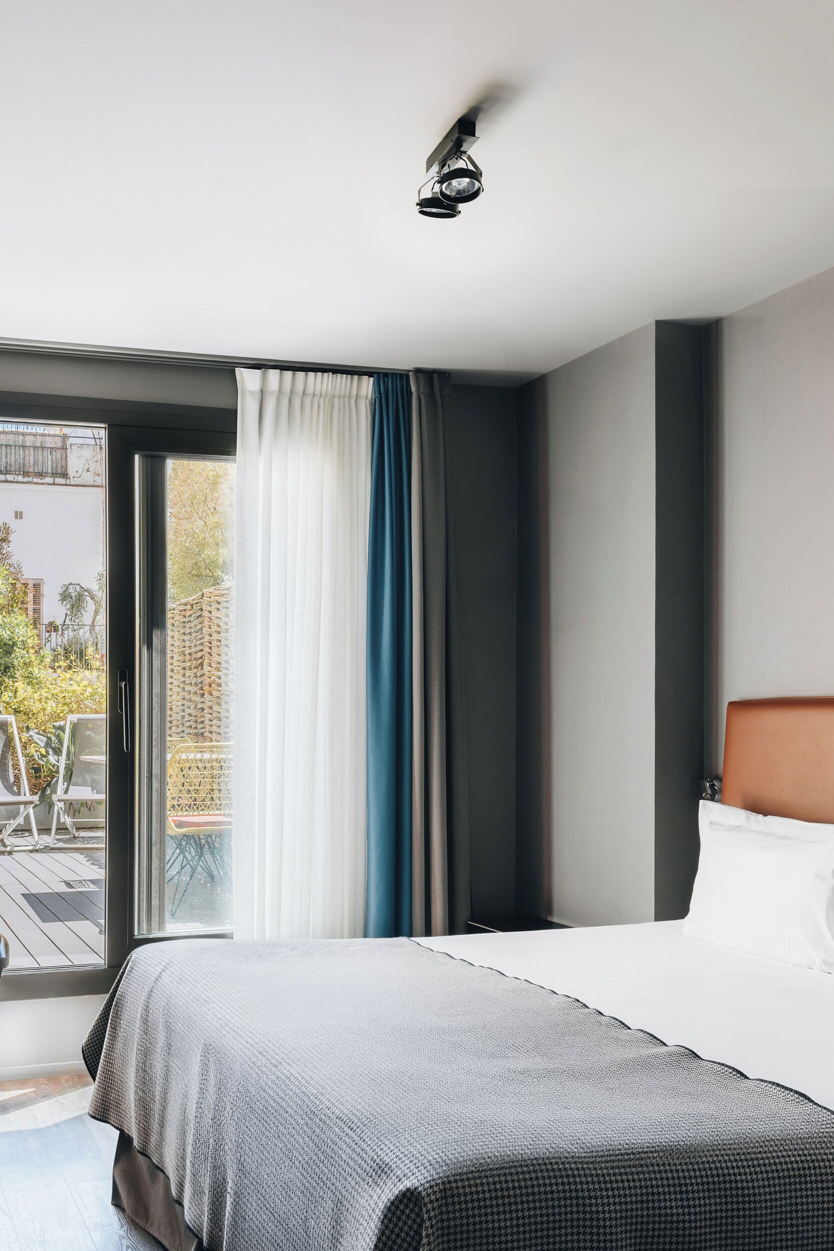 A hotel room with a bed, a window with curtains, a ceiling light, and a view of the outside.