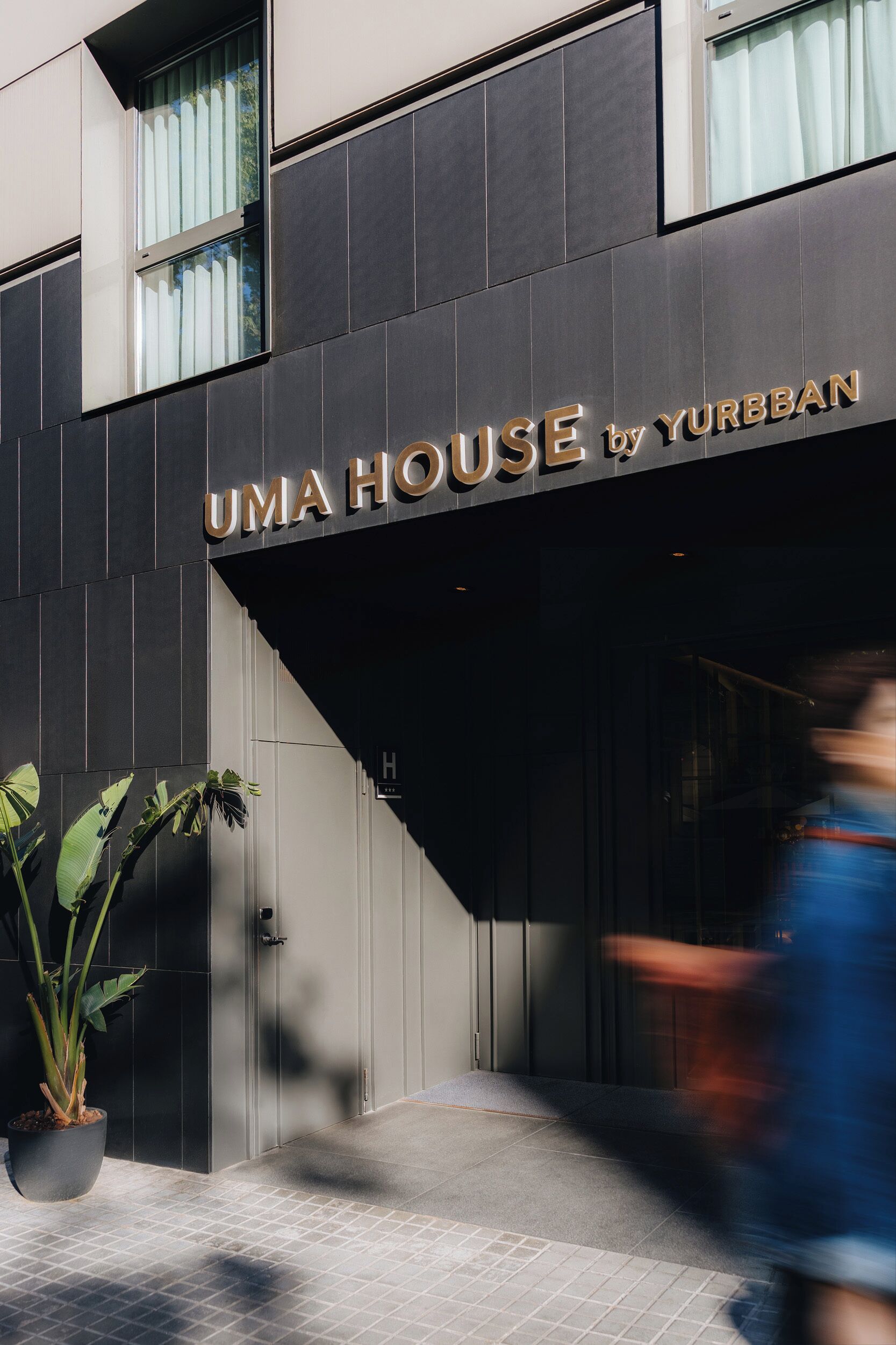 Un edificio con un letrero que dice 'UMA HOUSE by YURBBAN' y una planta en maceta en la entrada.