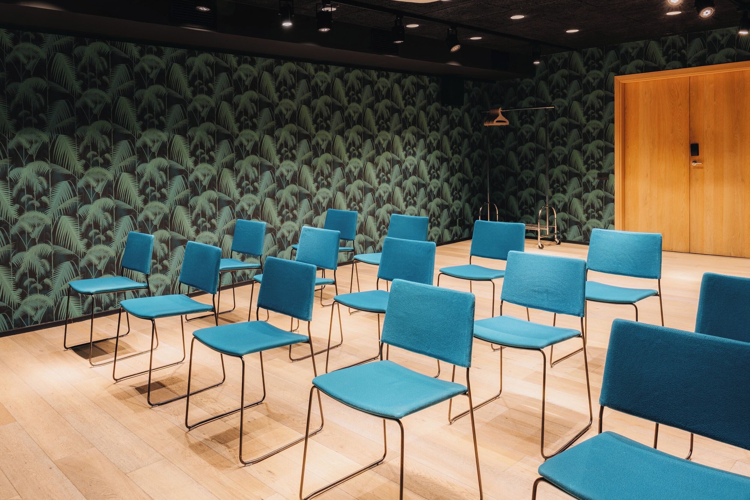 A room with rows of blue chairs, a wooden door, and a patterned wall.