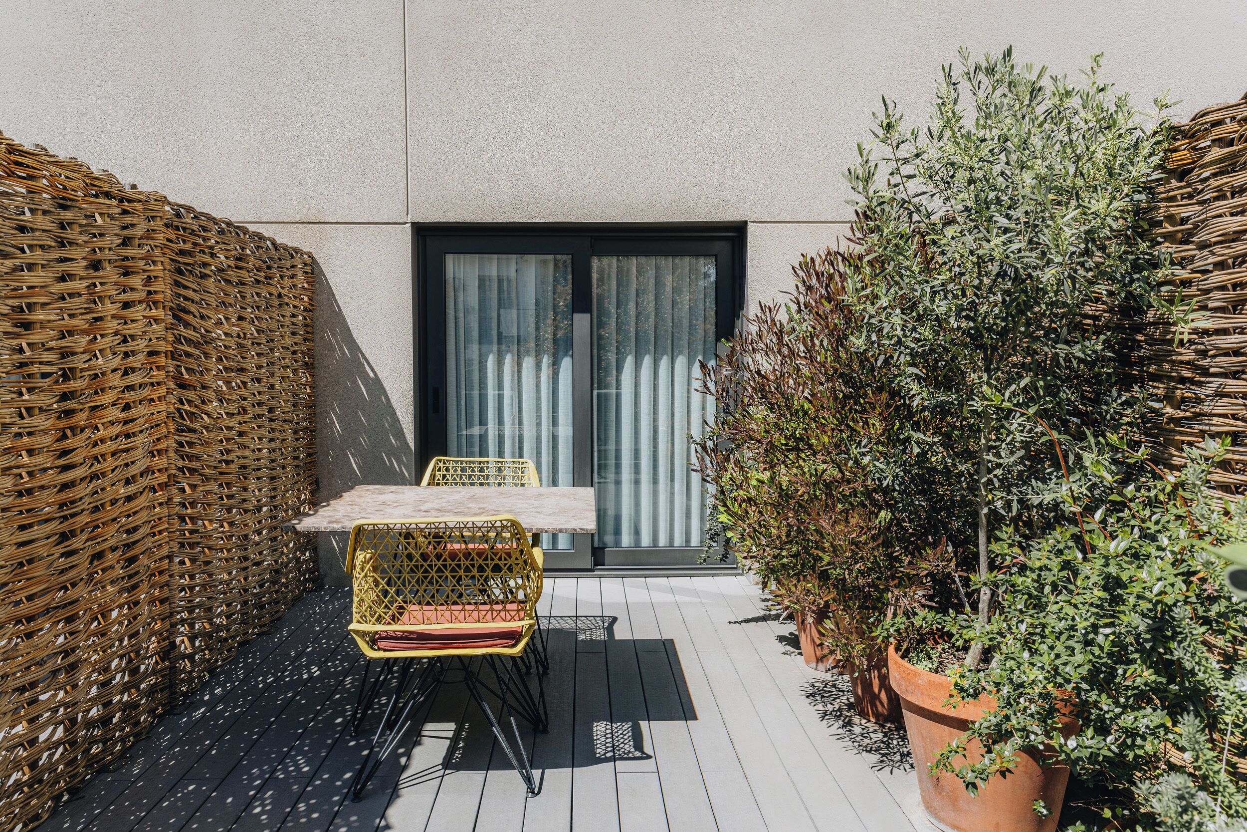 A small outdoor patio with a table and chairs, a wicker wall, and potted plants.