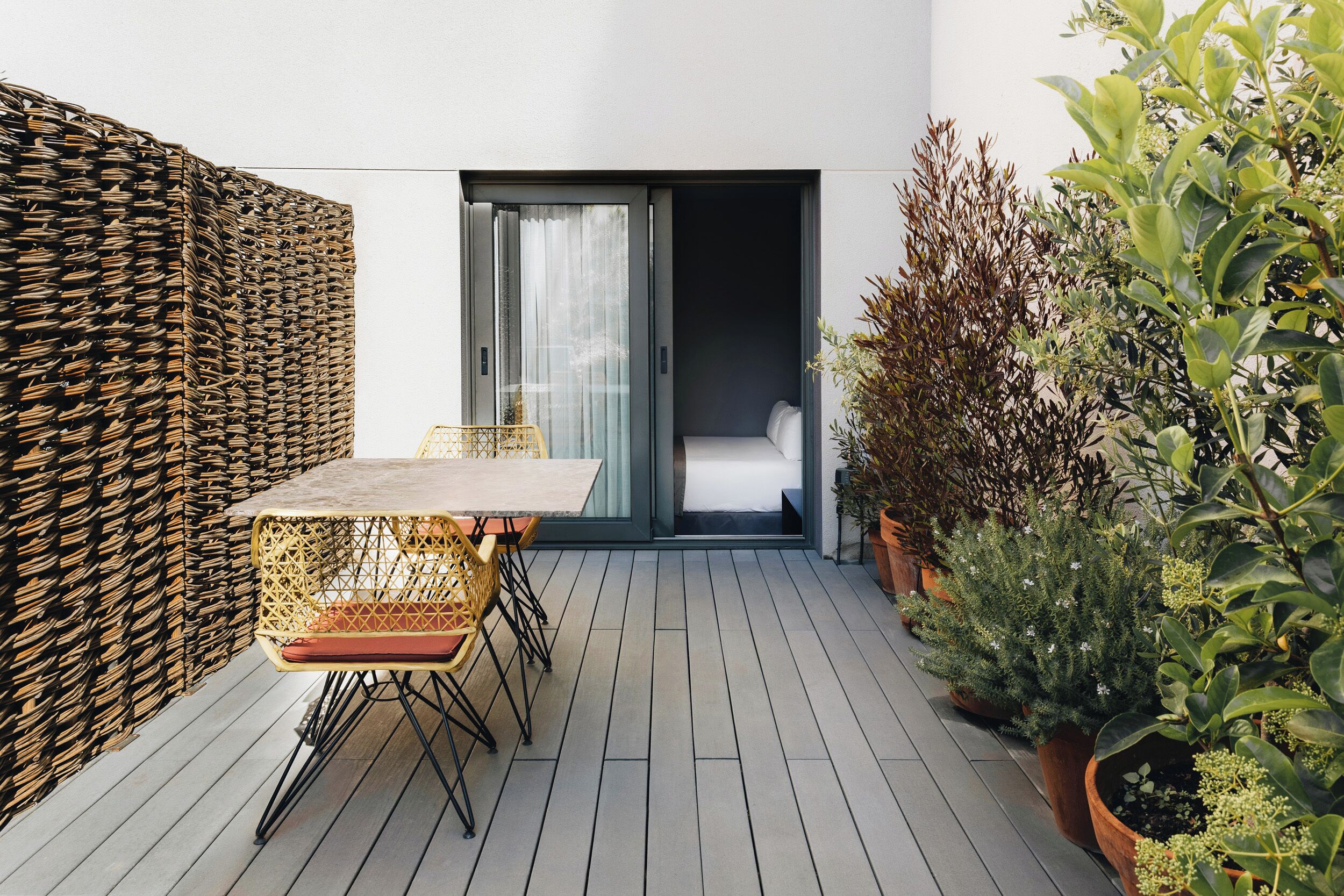 Un patio con una mesa y sillas, un muro de mimbre y plantas en macetas.