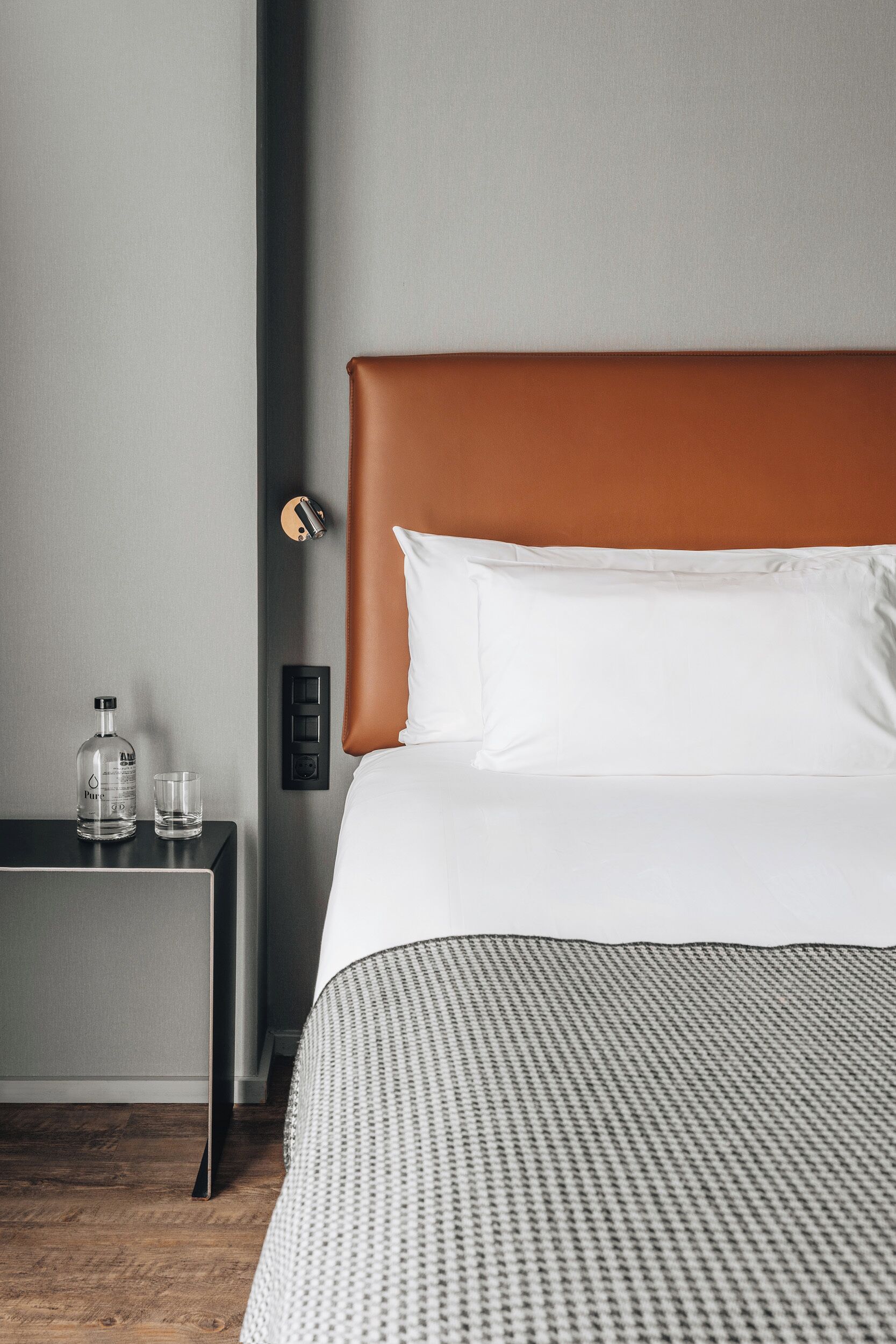 Una habitación de hotel ordenada con una cama, una mesita de noche, una botella y un vaso.
