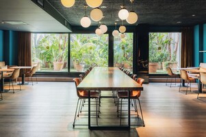 A conference room with a long table and chairs, large windows with a view of greenery, and pendant lighting.