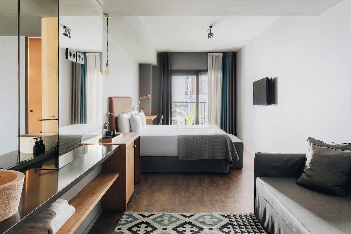 Een moderne hotelkamer met een groot bed, een bank, een spiegel, een houten bureau en uitzicht op buiten.