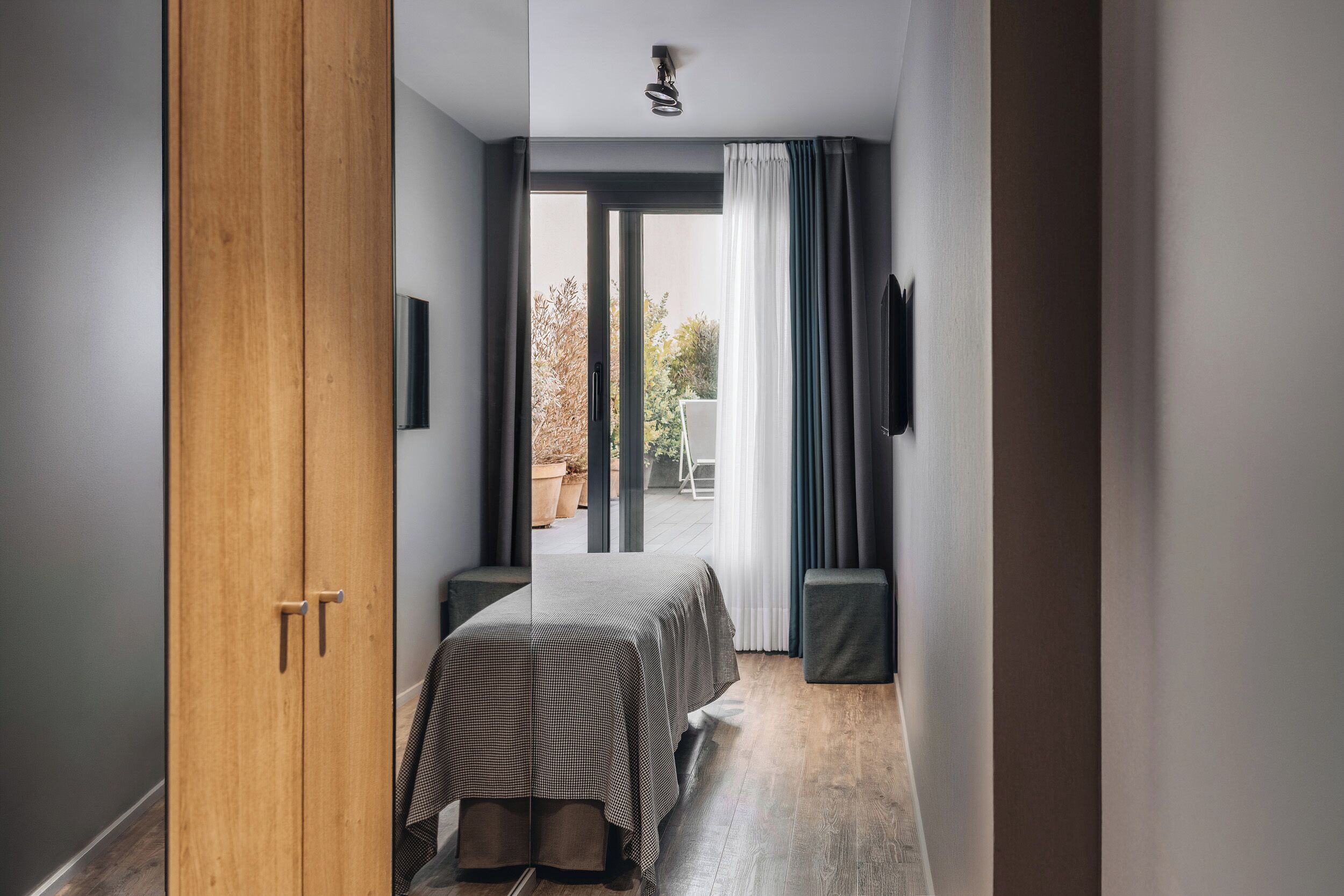 Um quarto com cama, guarda-roupa de madeira, televisão e janela com cortinas.