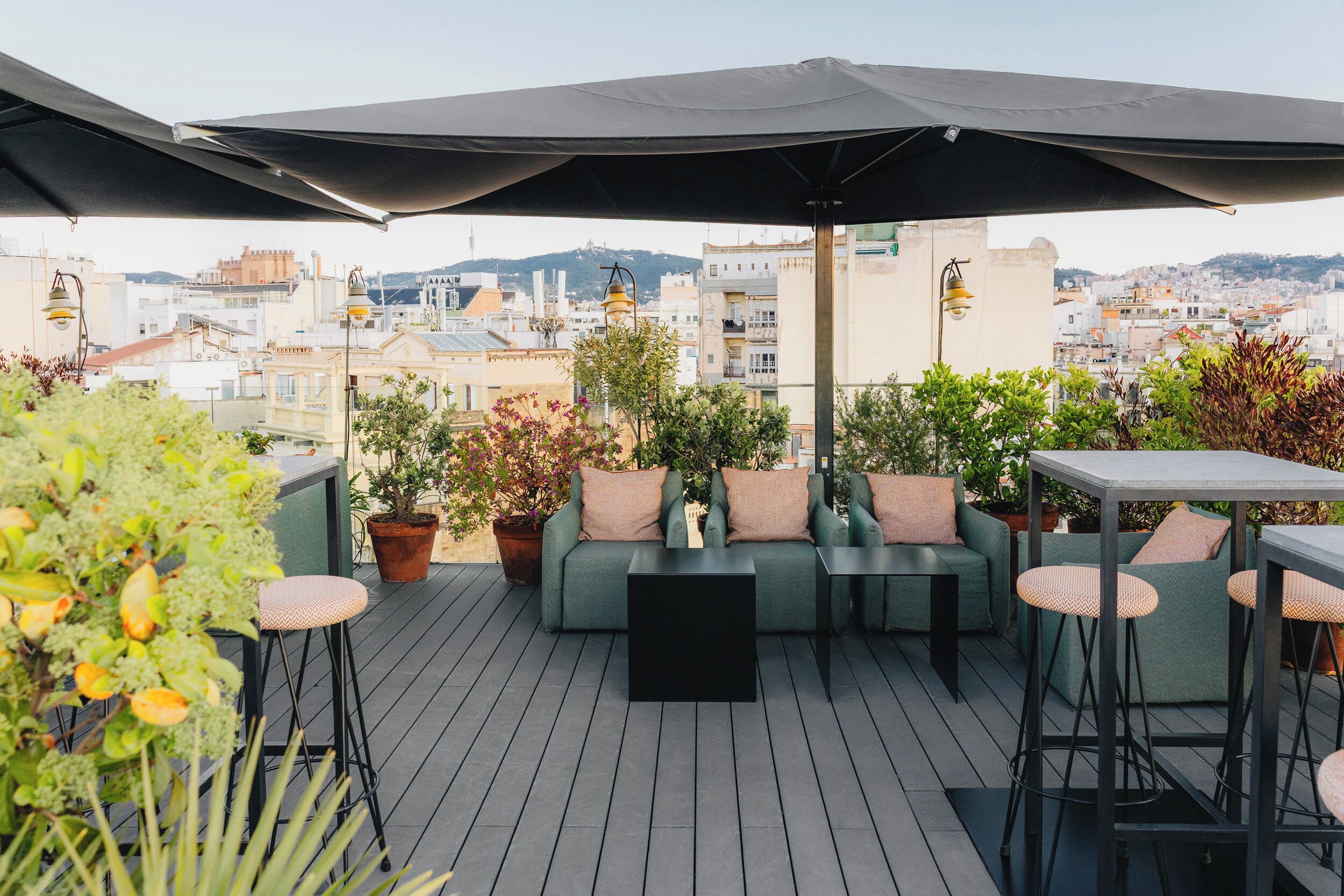 An outdoor seating area with a sofa, chairs, and a table, surrounded by potted plants and overlooking a cityscape.