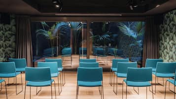 Una sala conferenze con file di sedie, un proiettore e vista su piante tropicali attraverso ampie finestre.