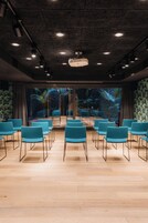 Una sala conferenze con file di sedie, un proiettore e vista su piante tropicali attraverso ampie finestre.