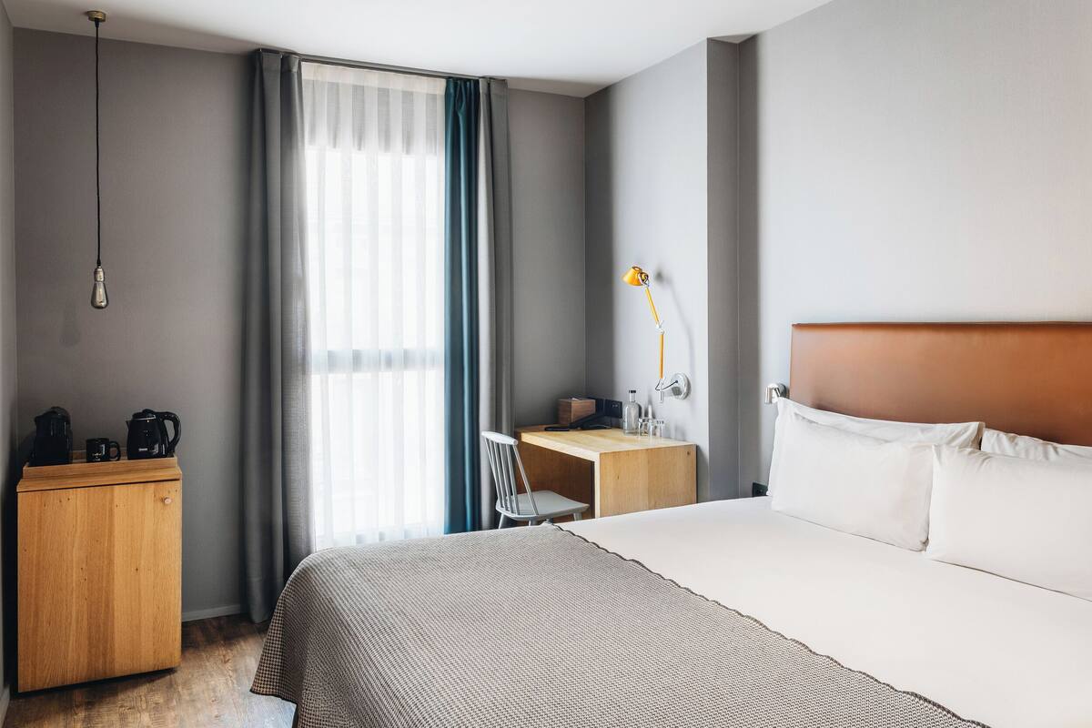 Een hotelkamer met een bed, een bureau, een stoel, een lamp en een kledingkast.