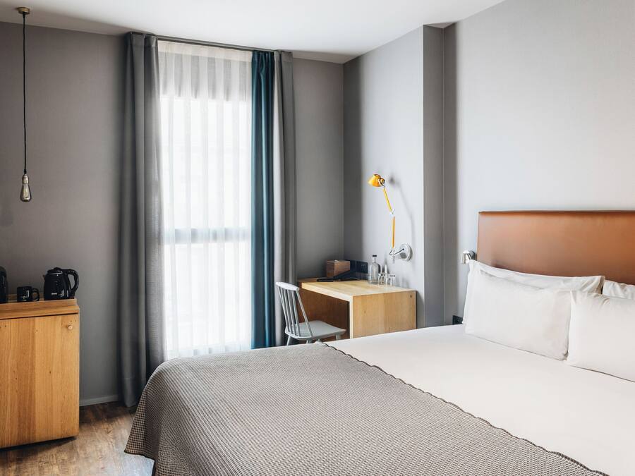 Una habitación de hotel con cama, escritorio, silla, lámpara y armario.