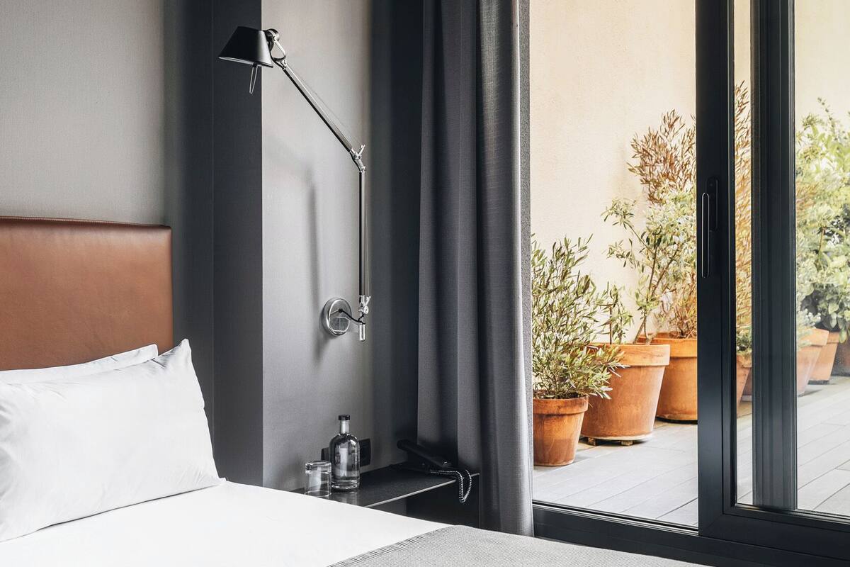 Een hotelkamer met een bed, nachtkastje, lamp en groot raam met gordijnen.