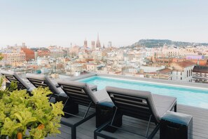 Une piscine sur le toit, dotée de chaises longues et offrant une vue sur la ville.