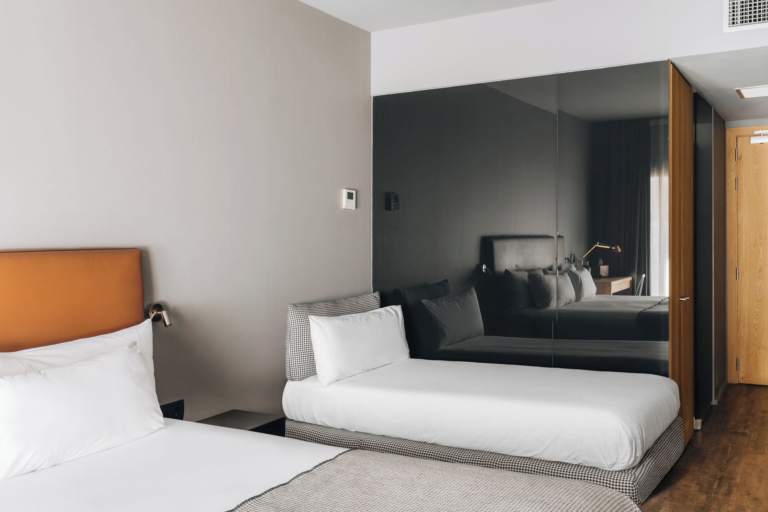 A hotel room with a large bed, a smaller bed, a mirror, and a wooden door.