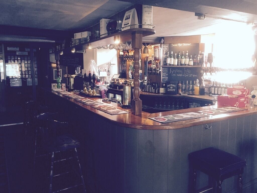 Eine Bar mit Theke, Hockstühlen und Regalen voller Flaschen.