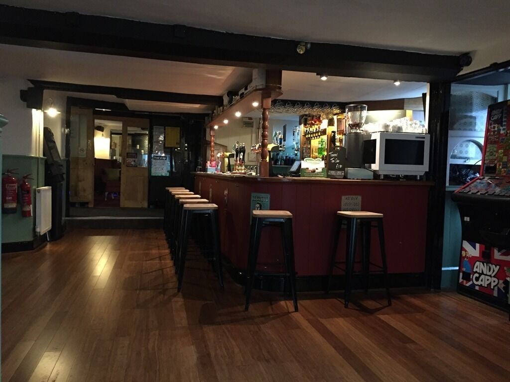 A bar area with stools, a counter, and a television. There are signs on the counter and a fire extinguisher on the wall.