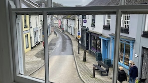 A street view through a window with buildings, a pedestrian, and a bench. - The Globe Inn (Buckfastleigh)