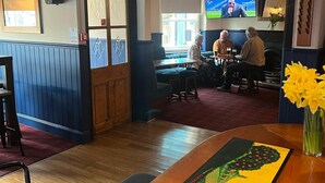 A bar area with wooden furniture, a television screen, and a cactus-themed table runner. - The Globe Inn (Buckfastleigh)