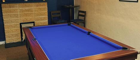 A pool table in a room with a television displaying a sports event, a framed picture on the wall, and a sign that reads "POOLROOM".
