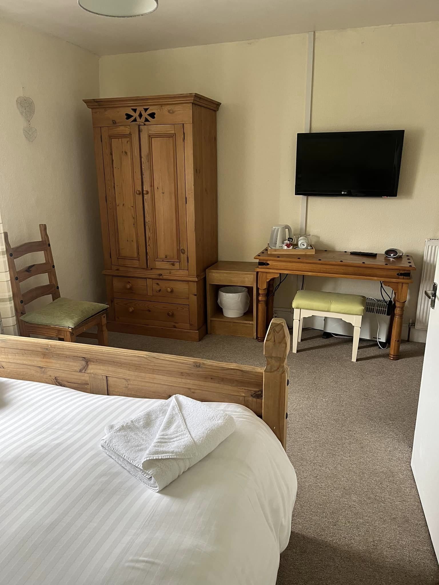 A bedroom with a wooden bed, a wooden wardrobe, a desk with a chair, a television, and a radiator.