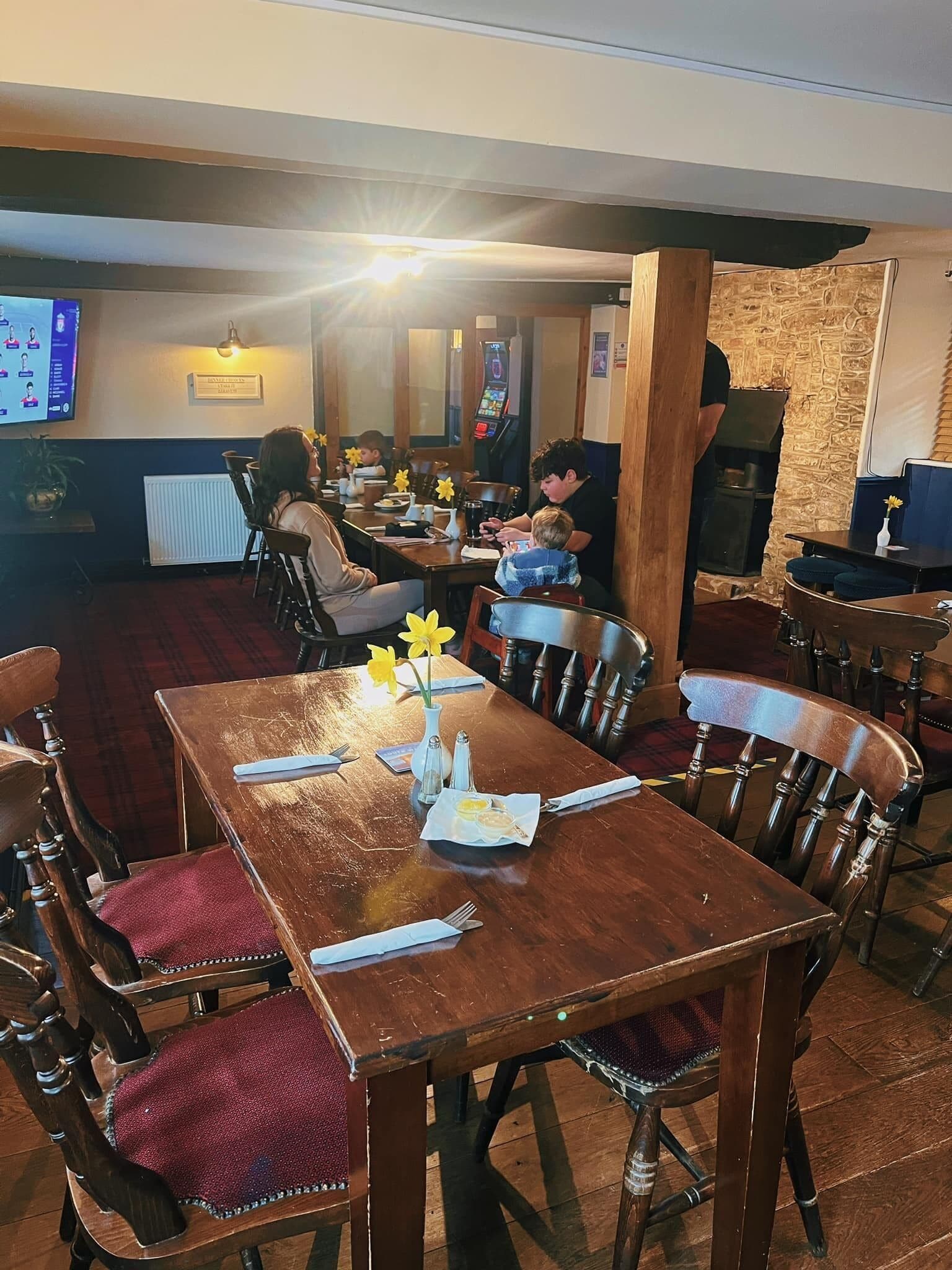 A restaurant with wooden tables and chairs, a stone wall, and a digital menu display.