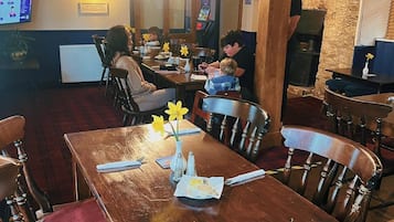 A restaurant with wooden tables and chairs, a stone wall, and a digital menu display.