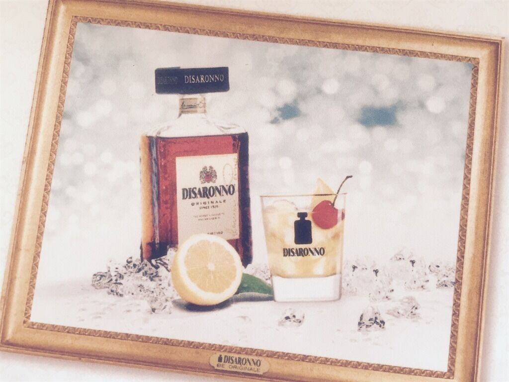 A framed picture of a bottle and a glass of DISARONNO with a lemon slice and cherry.