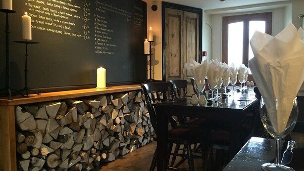 A restaurant with a blackboard menu, wooden log wall, and a table set with white napkins and wine glasses. - The Globe Inn (Buckfastleigh)