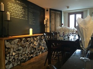 Un restaurante con un menú en una pizarra, pared de troncos de madera y una mesa dispuesta con servilletas blancas y copas de vino.