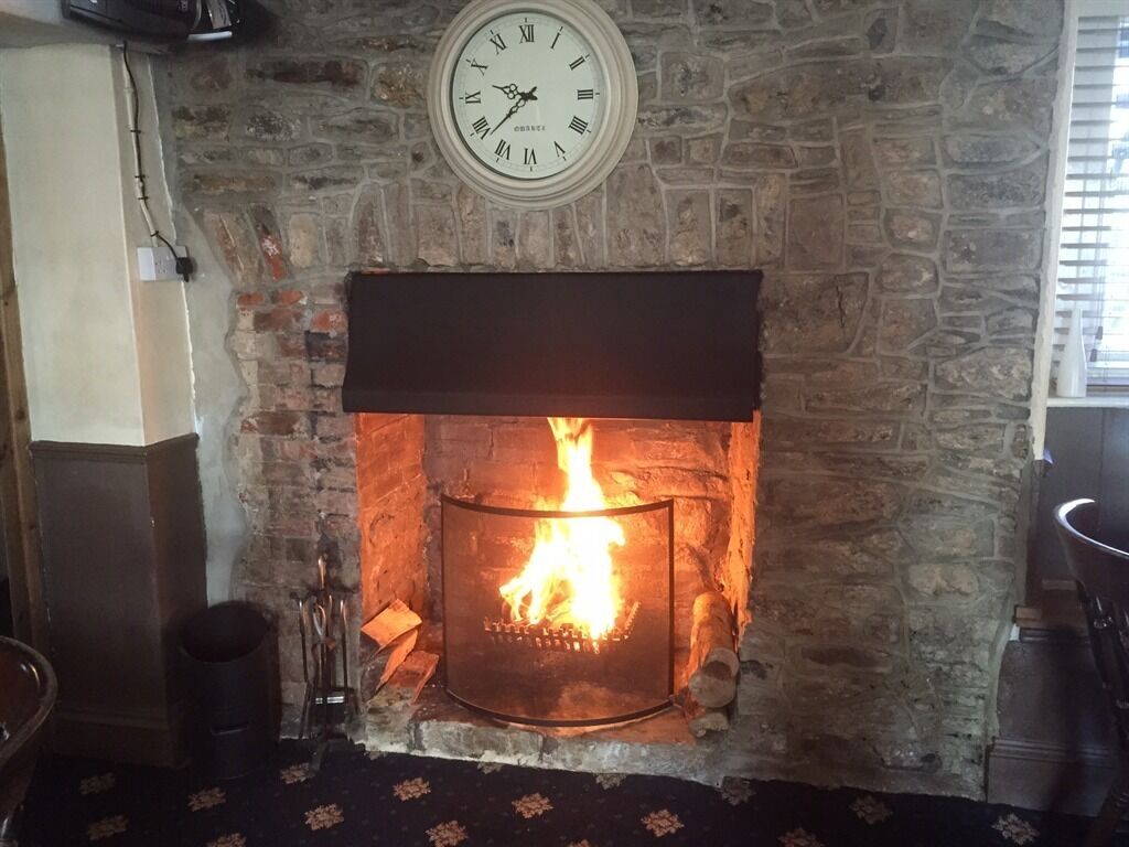 A stone fireplace with a clock above it, a fire burning inside, and a window to the right.