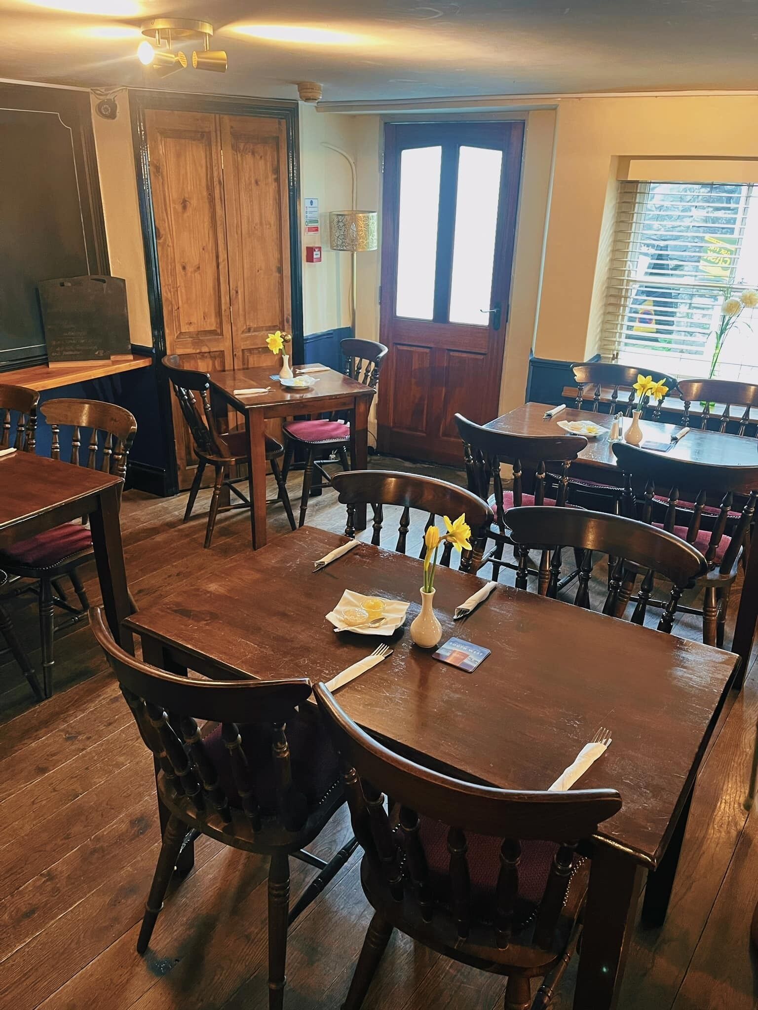 A dining area with wooden tables and chairs, a wooden door, and a window with blinds.