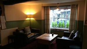 A cozy room with a leather sofa, a wooden coffee table, and a window with curtains. - The Globe Inn (Buckfastleigh)