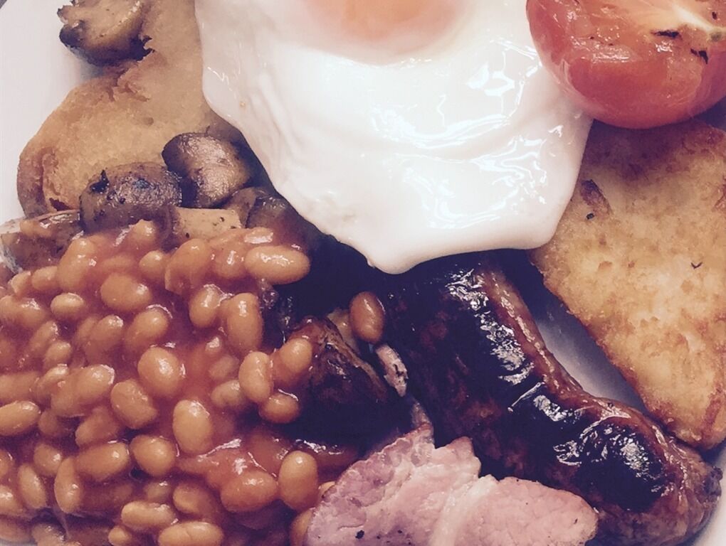 Ein Frühstücksteller mit Eiern, Bohnen, Würstchen und Rösti.