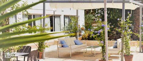 An outdoor patio area with a covered seating area, a table, and potted plants.