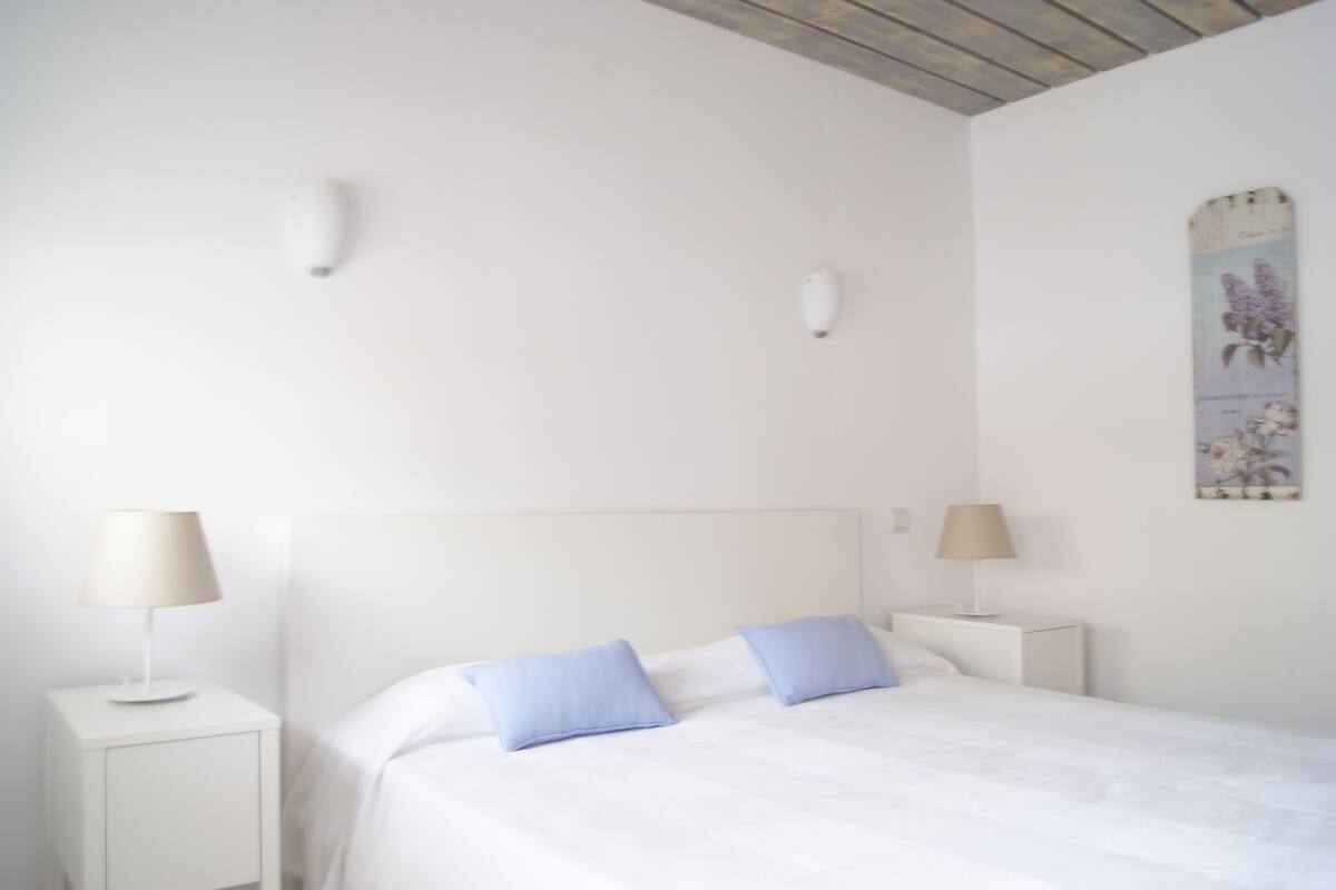 A bedroom with a white bed, two nightstands, and a wooden ceiling.