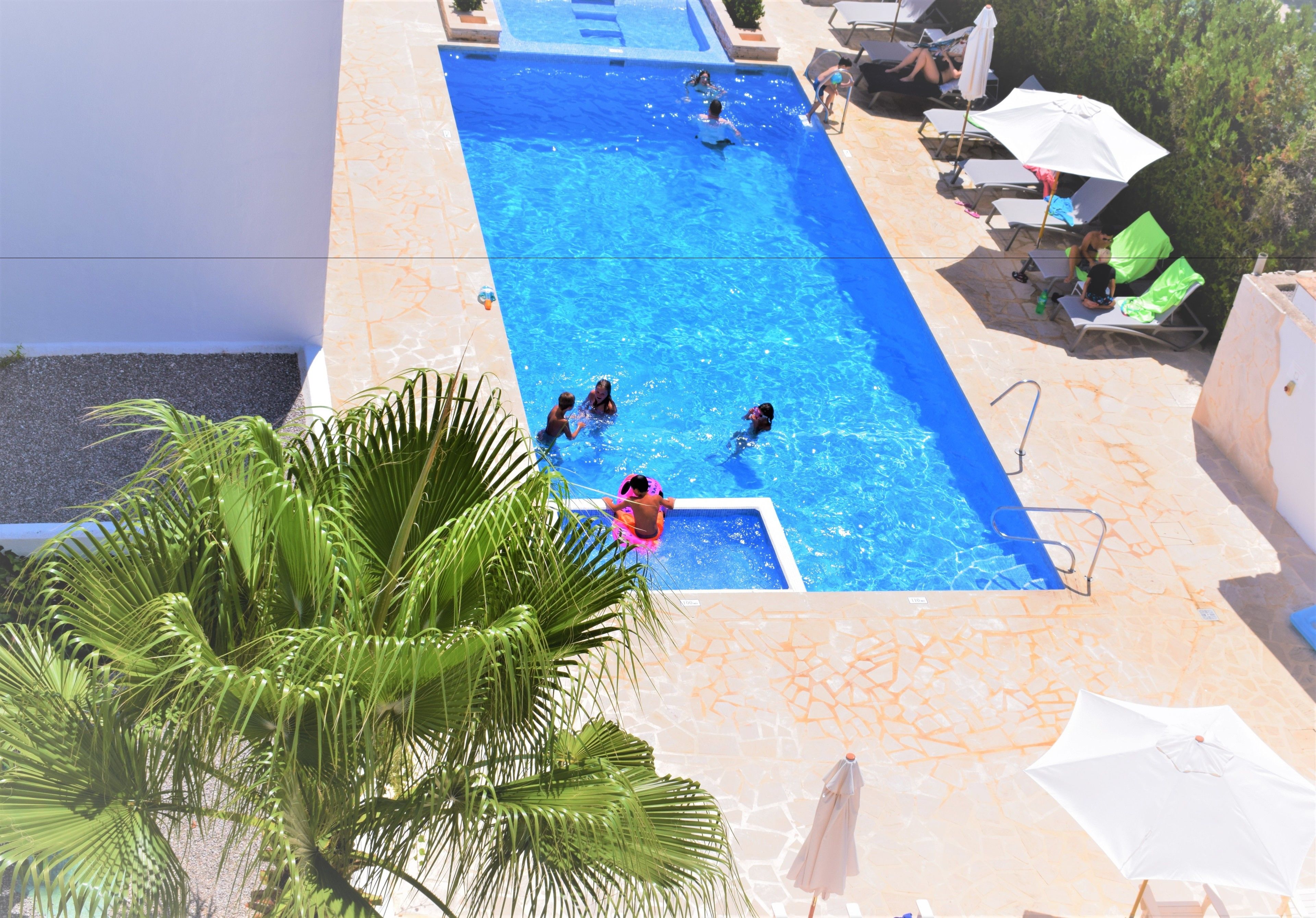 Una piscina con gente nadando y tomando el sol.