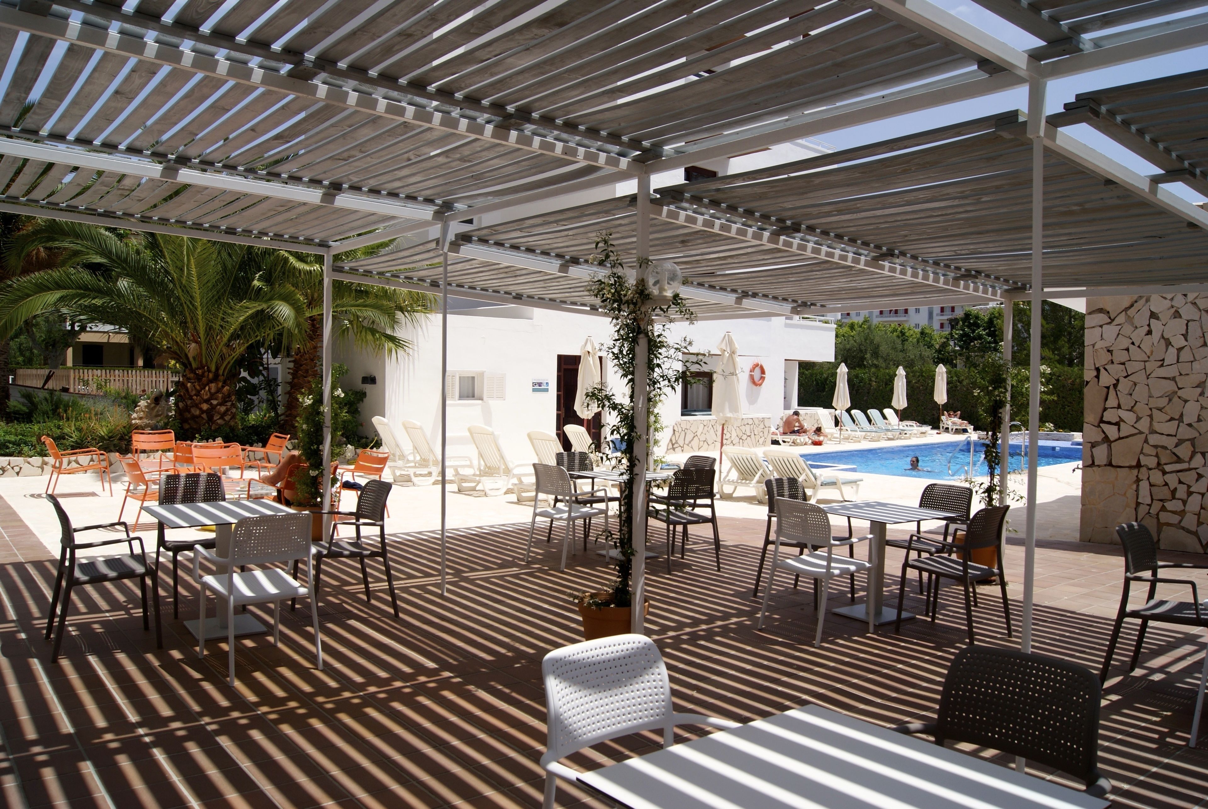 Un espace extérieur abrité, doté de tables et de chaises, d’une piscine et d’un mur en pierre.