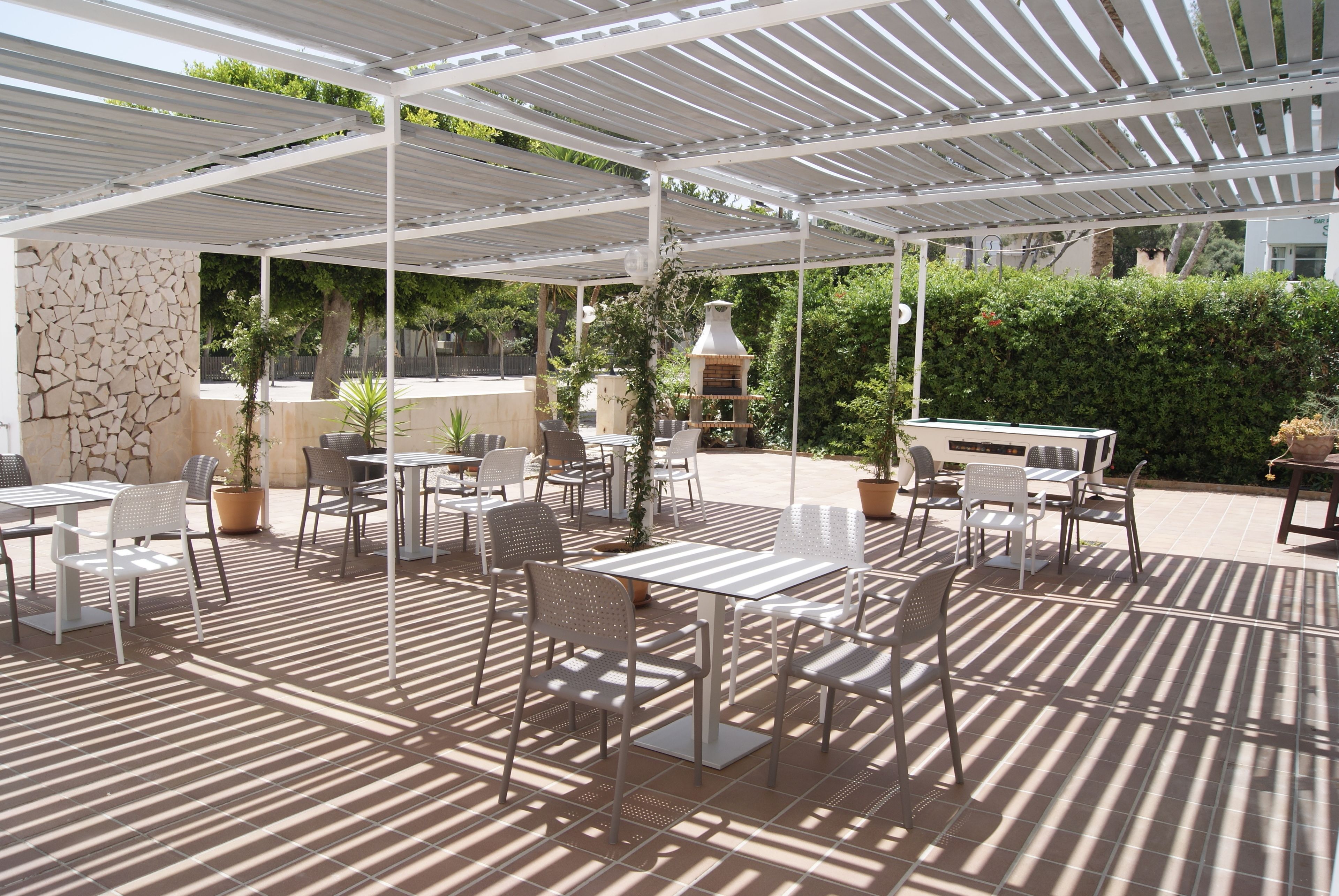 An outdoor patio with tables and chairs, a stone wall, and a pergola.
