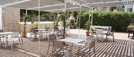 An outdoor patio with tables and chairs, a stone wall, and a pergola.