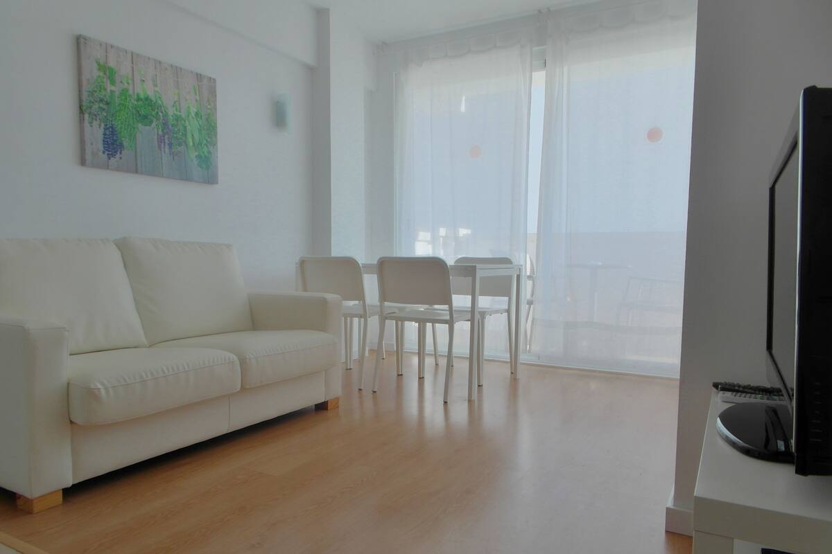 A modern living room with a white sofa, two white chairs, a small table, and a TV on a stand.