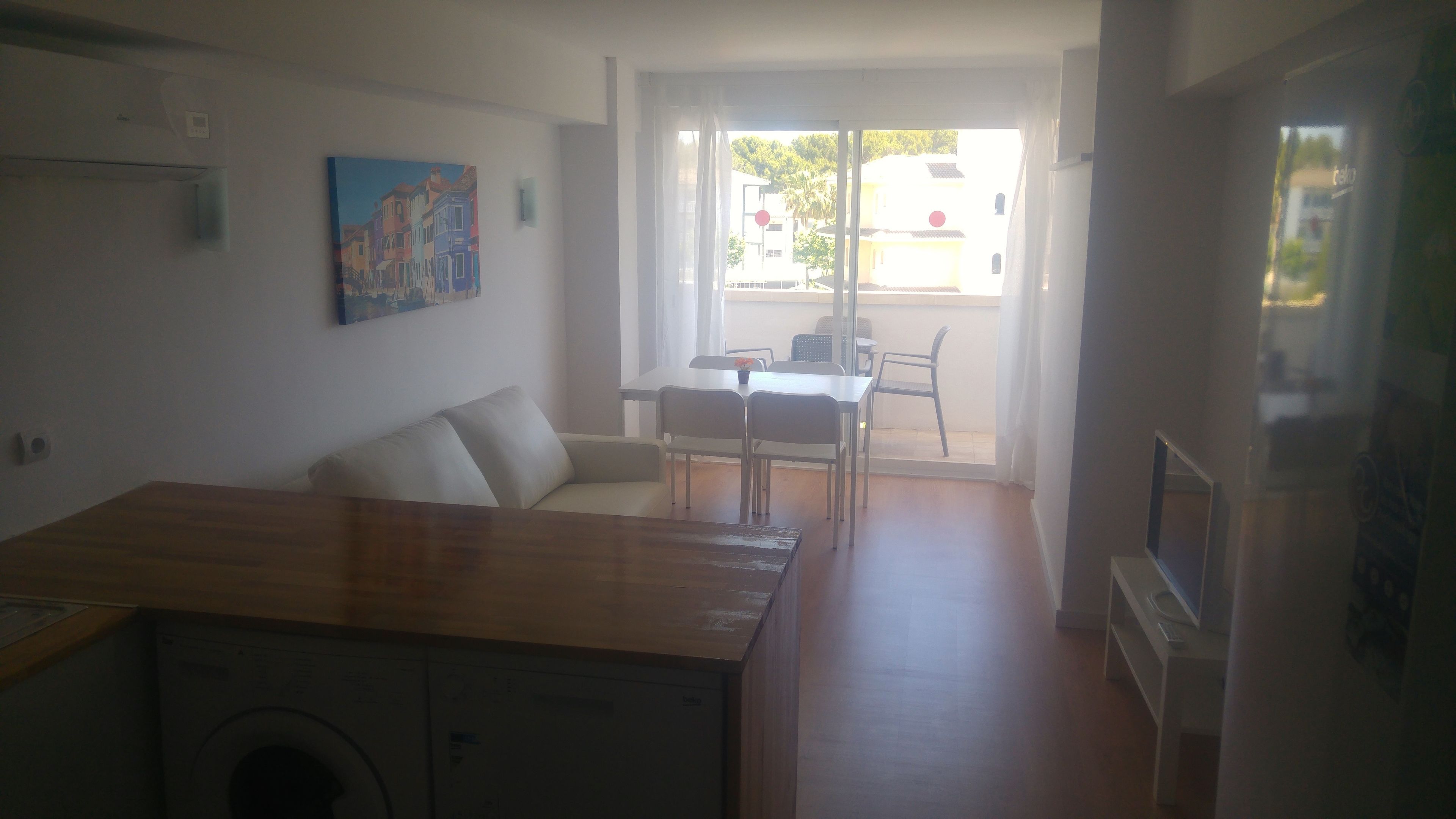En kompakt opholdsstue med tekøkken, spiseplads med bord og stole, samt udsigt ud af en glasdør.