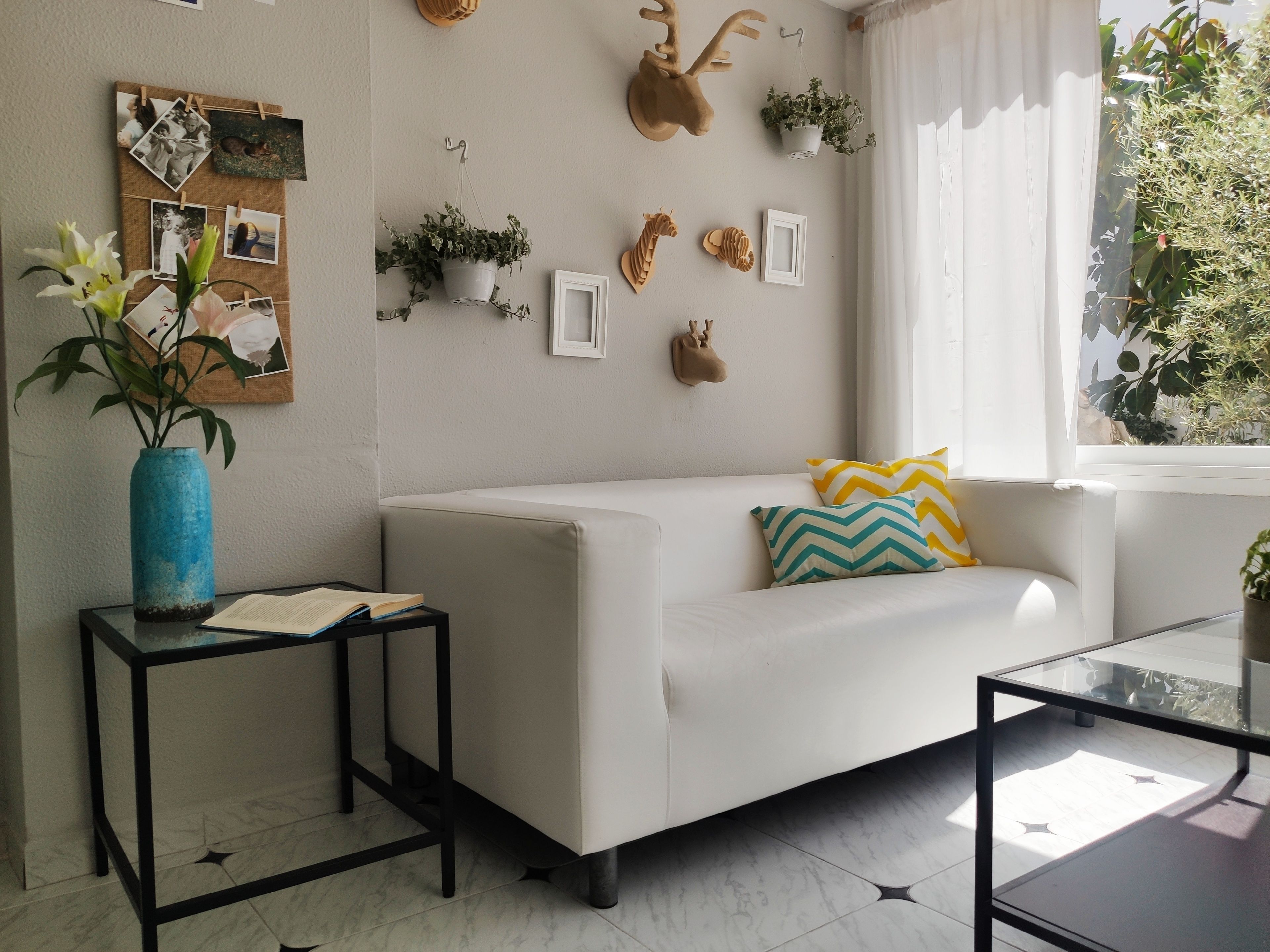 A modern living room with a white sofa, decorative wall art, and a variety of potted plants.