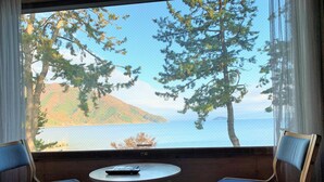 A room with two chairs and a small table, a window with a view of trees and a body of water. - Okubiwako Makino Grand Park Hotel (Takashima)