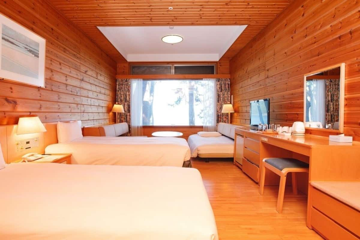 Quarto estilo cabana com duas camas, uma escrivaninha, uma cadeira e uma televisão.