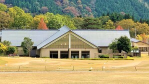 A building with a large glass facade and a sloped roof, surrounded by a grassy field and trees. - Okubiwako Makino Grand Park Hotel (Takashima)